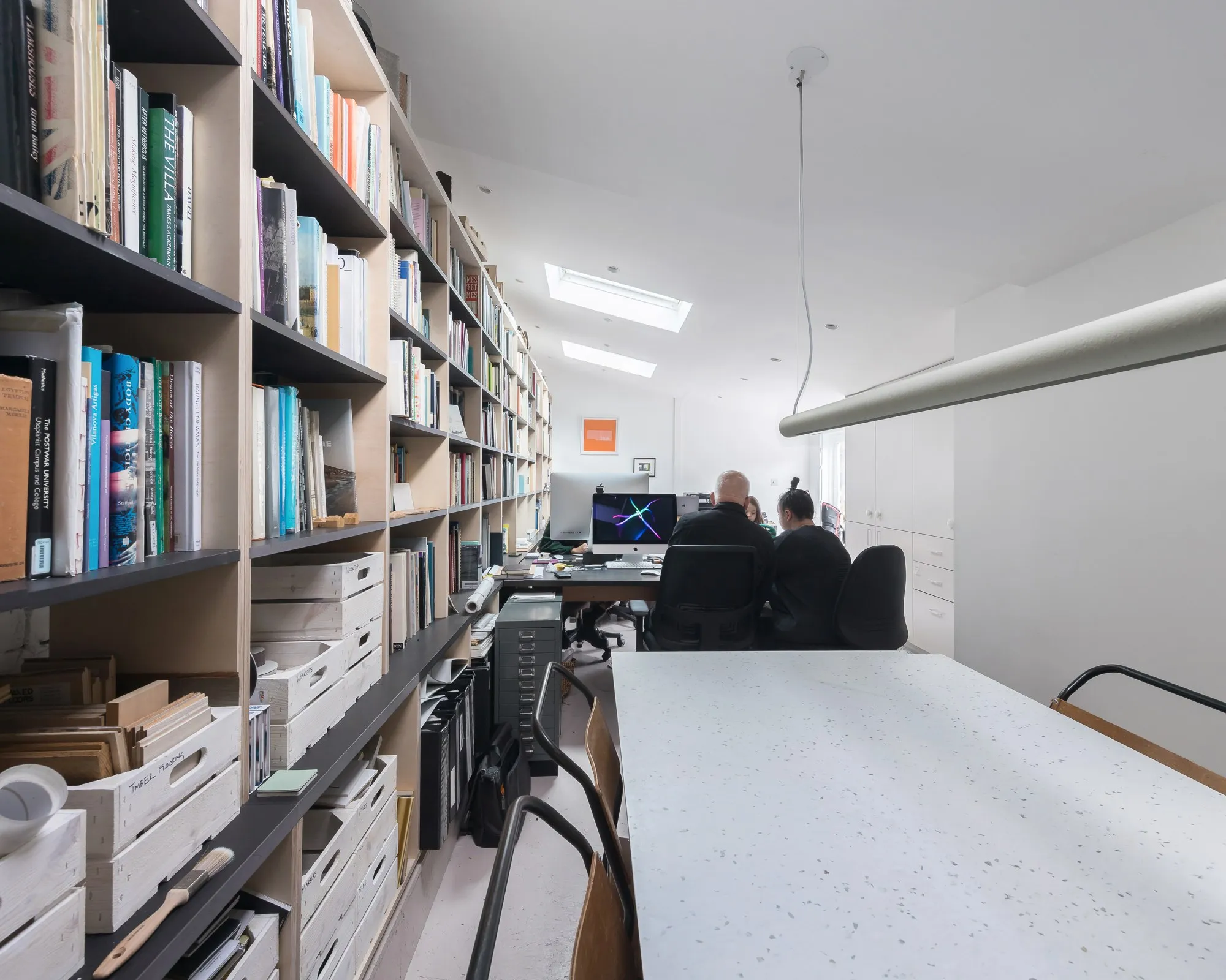 A wall of books beside a run of desks, in a studio at Hone Limehouse