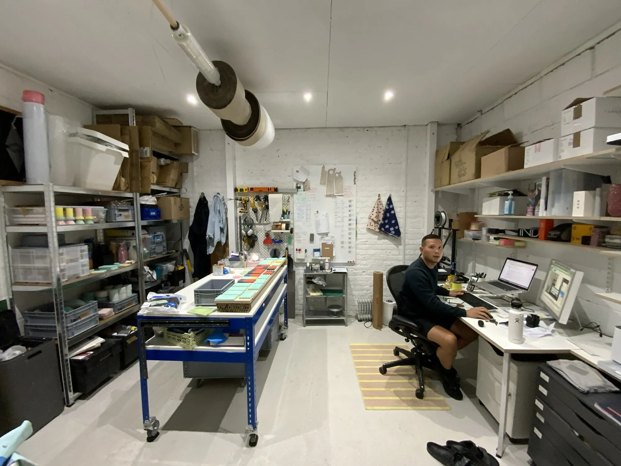 A maker at work among shelves of parts and tools, in a studio at Hone Limehouse